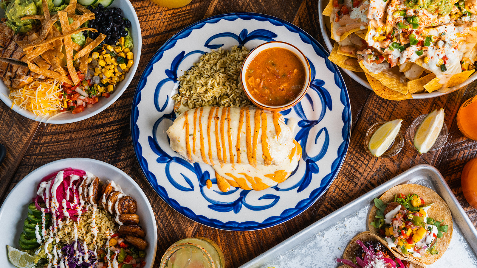 Burrito, nachos, tacos and a taco salad bowl spread across a table at Social Cantina